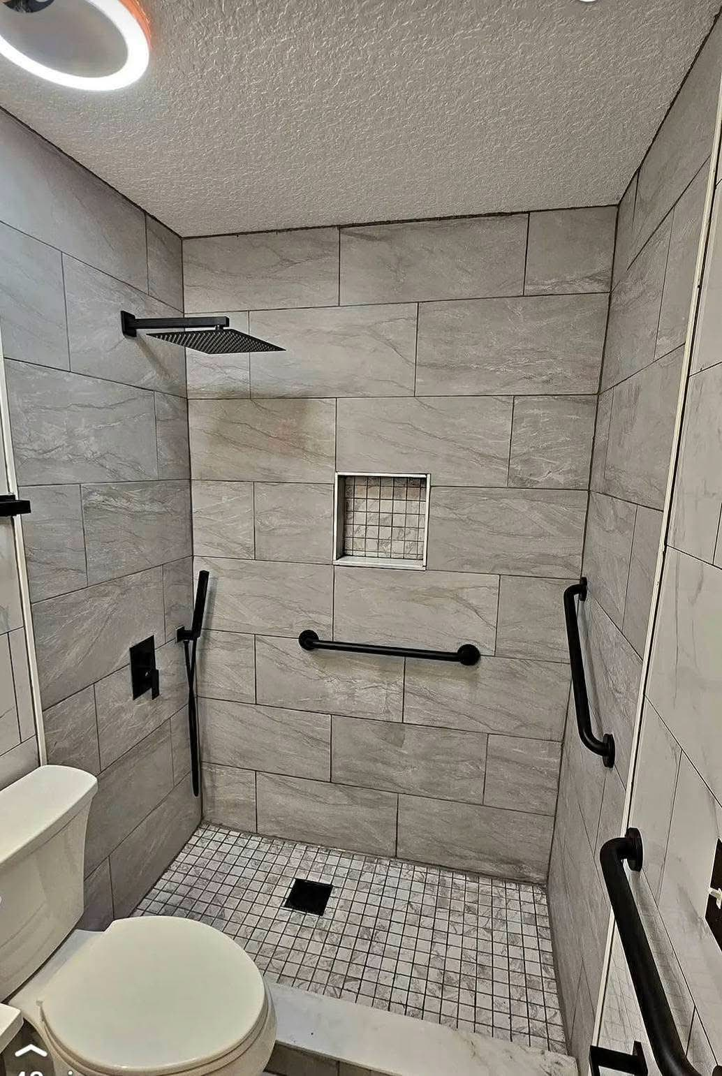 Gray porcelain walk-in shower with niche, grab bars and mosaic floor